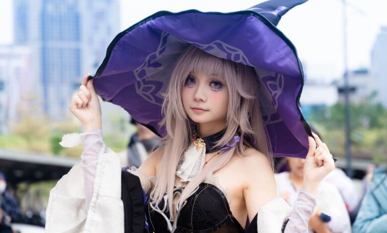 A young woman cosplaying as a witch outdoors, wearing a purple hat and fantasy attire.