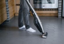 A person cleaning a tiled floor with a modern vacuum cleaner indoors.