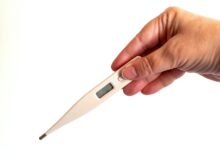 Close-up of a hand holding a digital thermometer, ideal for health and medical concepts.