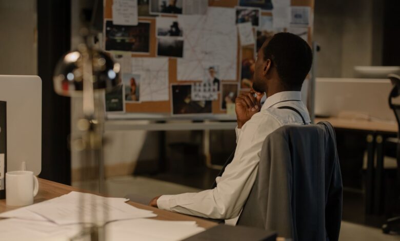 Detective in thought examining evidence board in a dimly lit office environment.