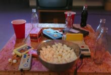 A nostalgic setup with popcorn, VHS tapes, and retro gaming consoles on a wooden table.