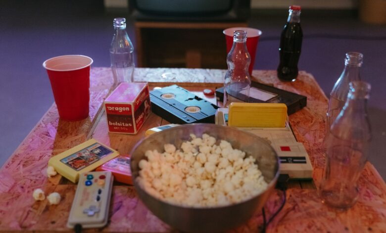 A nostalgic setup with popcorn, VHS tapes, and retro gaming consoles on a wooden table.