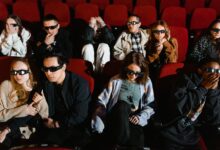 Group of people watching a movie in 3D glasses, expressing excitement and surprise.