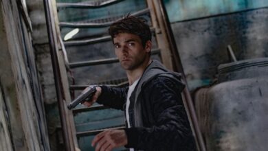 A man holding a gun in a dimly lit, mysterious urban setting.