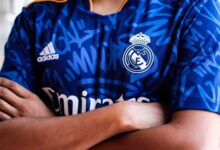 Arms crossed in a vibrant blue sports jersey with team logo and abstract pattern design.