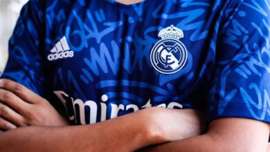 Arms crossed in a vibrant blue sports jersey with team logo and abstract pattern design.