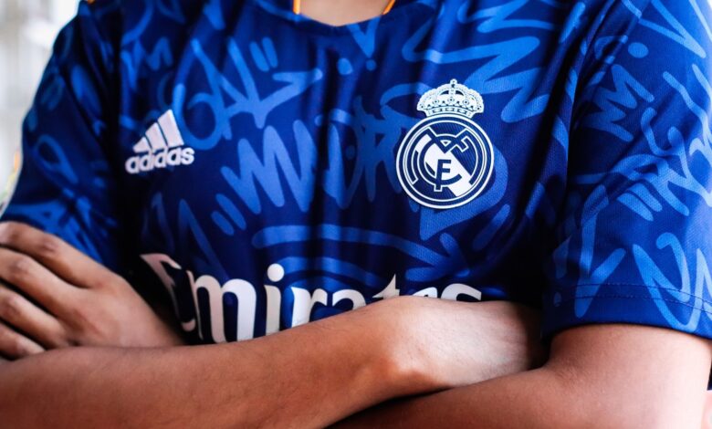 Arms crossed in a vibrant blue sports jersey with team logo and abstract pattern design.