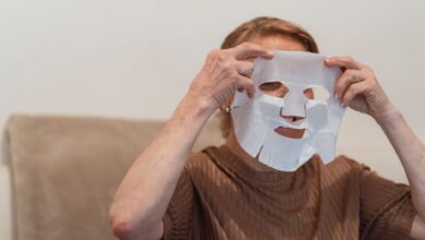 Senior woman applying a sheet face mask for skincare and relaxation indoors.