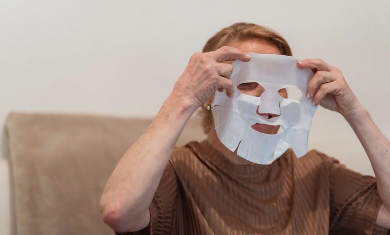 Senior woman applying a sheet face mask for skincare and relaxation indoors.