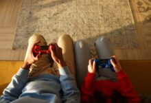 Two individuals using game controllers while sitting on a yellow couch, focused on gaming.