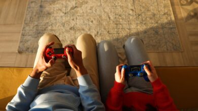 Two individuals using game controllers while sitting on a yellow couch, focused on gaming.