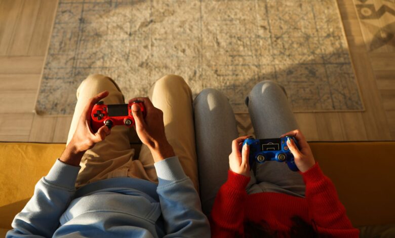 Two individuals using game controllers while sitting on a yellow couch, focused on gaming.