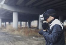 Man wearing VR headset under a bridge, exploring virtual reality outdoors.