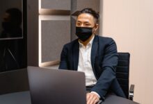 Professional businessman in formal attire wearing a face mask while working on a laptop in an office.