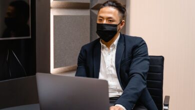 Professional businessman in formal attire wearing a face mask while working on a laptop in an office.