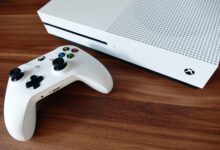 Close-up of a white Xbox console and controller on a wooden surface, ideal for gaming enthusiasts.