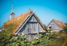 Exterior of lumber shed and church among lush green plants in traditional Norstead Viking Village against cloudless blue sky