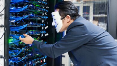 Masked individual interacting with server racks, symbolizing cybersecurity threats.