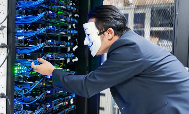 Masked individual interacting with server racks, symbolizing cybersecurity threats.