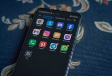 Close-up of a smartphone displaying popular social media apps on a floral fabric surface.