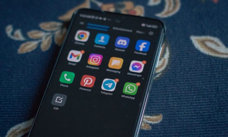 Close-up of a smartphone displaying popular social media apps on a floral fabric surface.