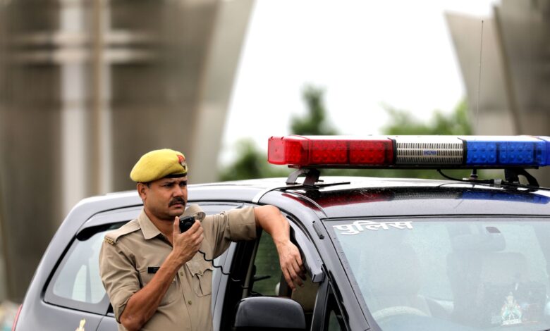 Police officer standing beside patrol car holding a radio microphone outdoors.