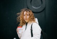 A woman with curly hair enjoying a warm coffee on a windy day in Glasgow.