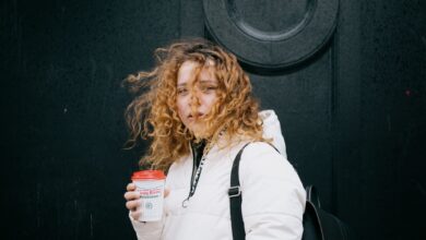 A woman with curly hair enjoying a warm coffee on a windy day in Glasgow.