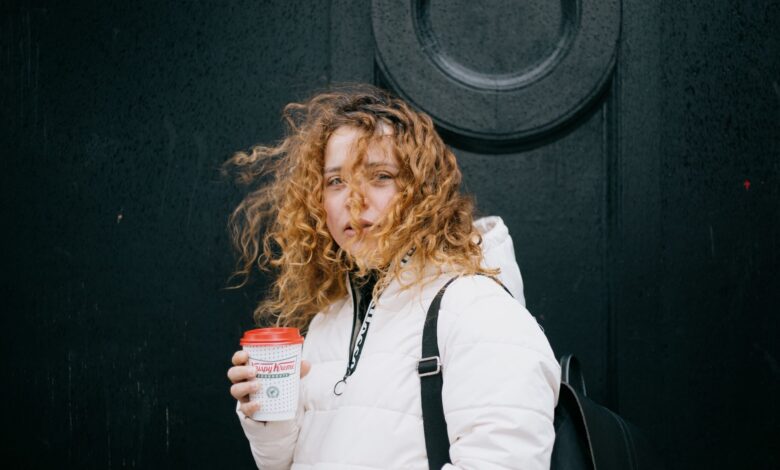 A woman with curly hair enjoying a warm coffee on a windy day in Glasgow.