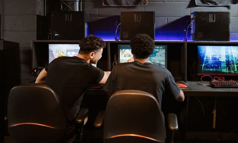 Two young men engaged in intense gaming session at an eSports venue. Computers and ambient lighting create an immersive experience.