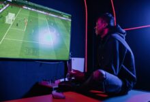 A young man enthusiastically playing video games on a console in a dimly lit gaming room.
