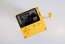 A yellow handheld gaming console featuring a crank handle on a white background.