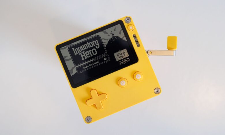A yellow handheld gaming console featuring a crank handle on a white background.