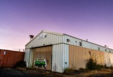 Abandoned corrugated warehouse with graffiti under a vibrant purple sky at twilight.
