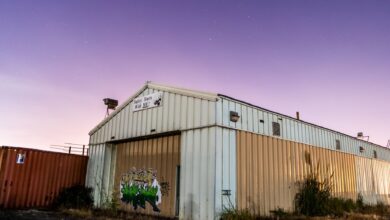 Abandoned corrugated warehouse with graffiti under a vibrant purple sky at twilight.