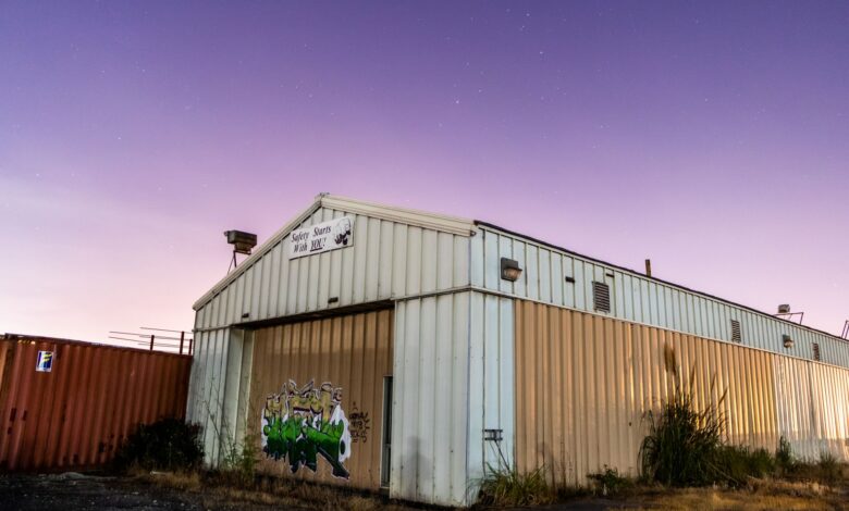 Abandoned corrugated warehouse with graffiti under a vibrant purple sky at twilight.