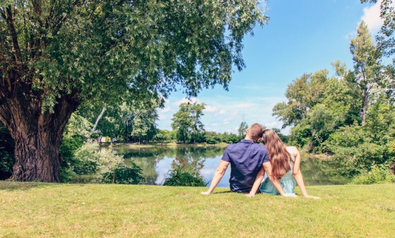 A couple sitting by a lake enjoying a sunny day in a lush park.
