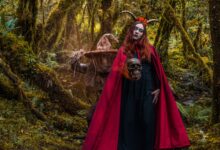 A woman in a witch costume with horns stands in a mystical forest in Colombia, holding a skull.
