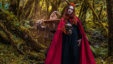 A woman in a witch costume with horns stands in a mystical forest in Colombia, holding a skull.