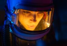 Close-up of a woman in a space suit under blue light, looking focused and futuristic.