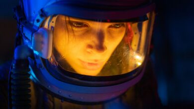 Close-up of a woman in a space suit under blue light, looking focused and futuristic.