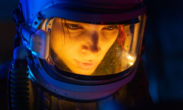 Close-up of a woman in a space suit under blue light, looking focused and futuristic.