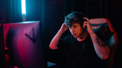Tattooed man focused on gaming with headset at night.