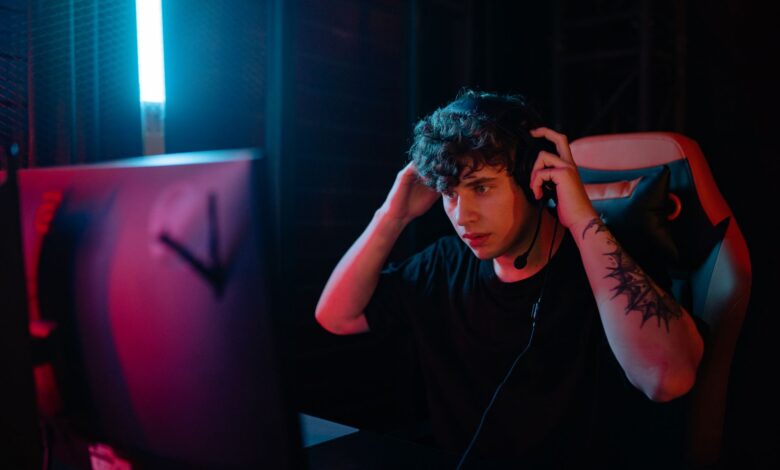 Tattooed man focused on gaming with headset at night.