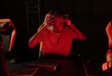 A young man enthusiastically gaming in a dimly lit room with headphones on.