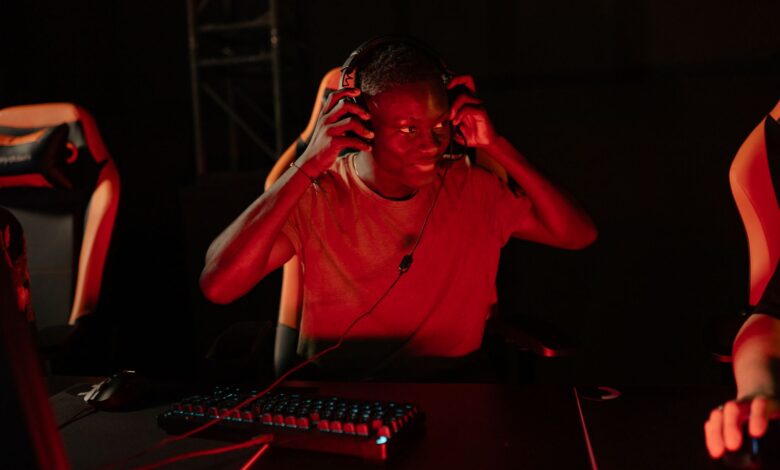 A young man enthusiastically gaming in a dimly lit room with headphones on.