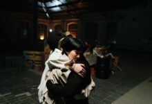 Two women share a warm hug in an industrial style indoor setting.