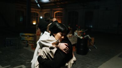 Two women share a warm hug in an industrial style indoor setting.