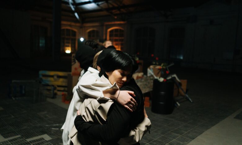 Two women share a warm hug in an industrial style indoor setting.