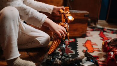A child in pajamas plays with a toy dinosaur on a colorful rug indoors.